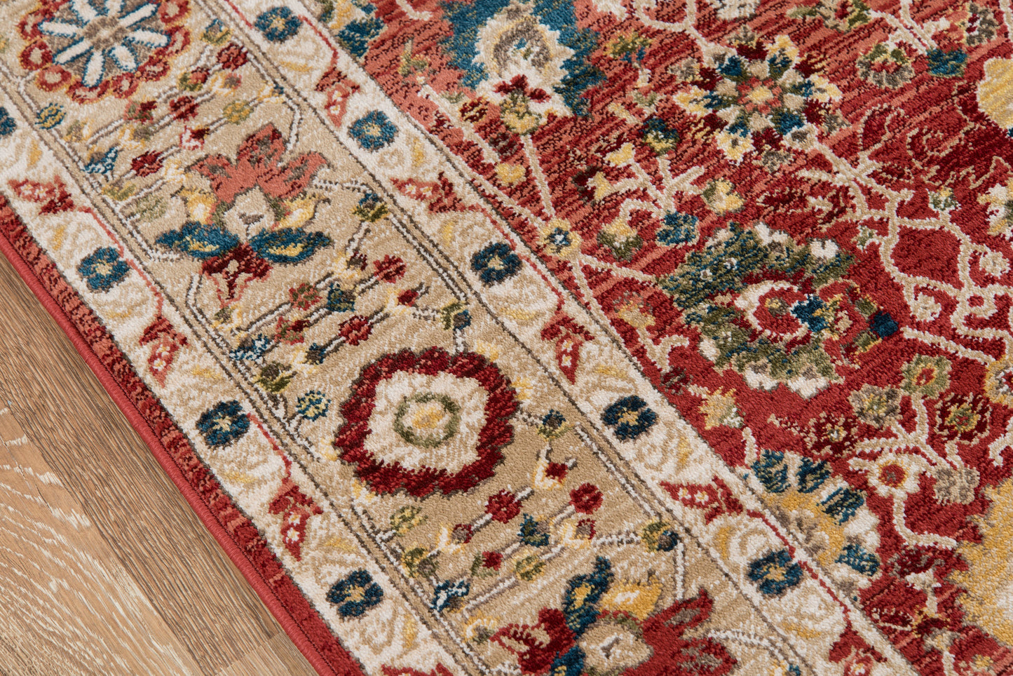 Rectangular oriental rug with red field, ivory border, blue & gold floral motifs on a wooden floor.