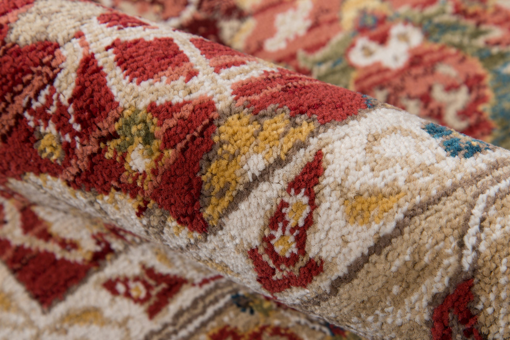 Close-up of a rolled oriental rug with red, cream, gold & blue motifs; plush pile.