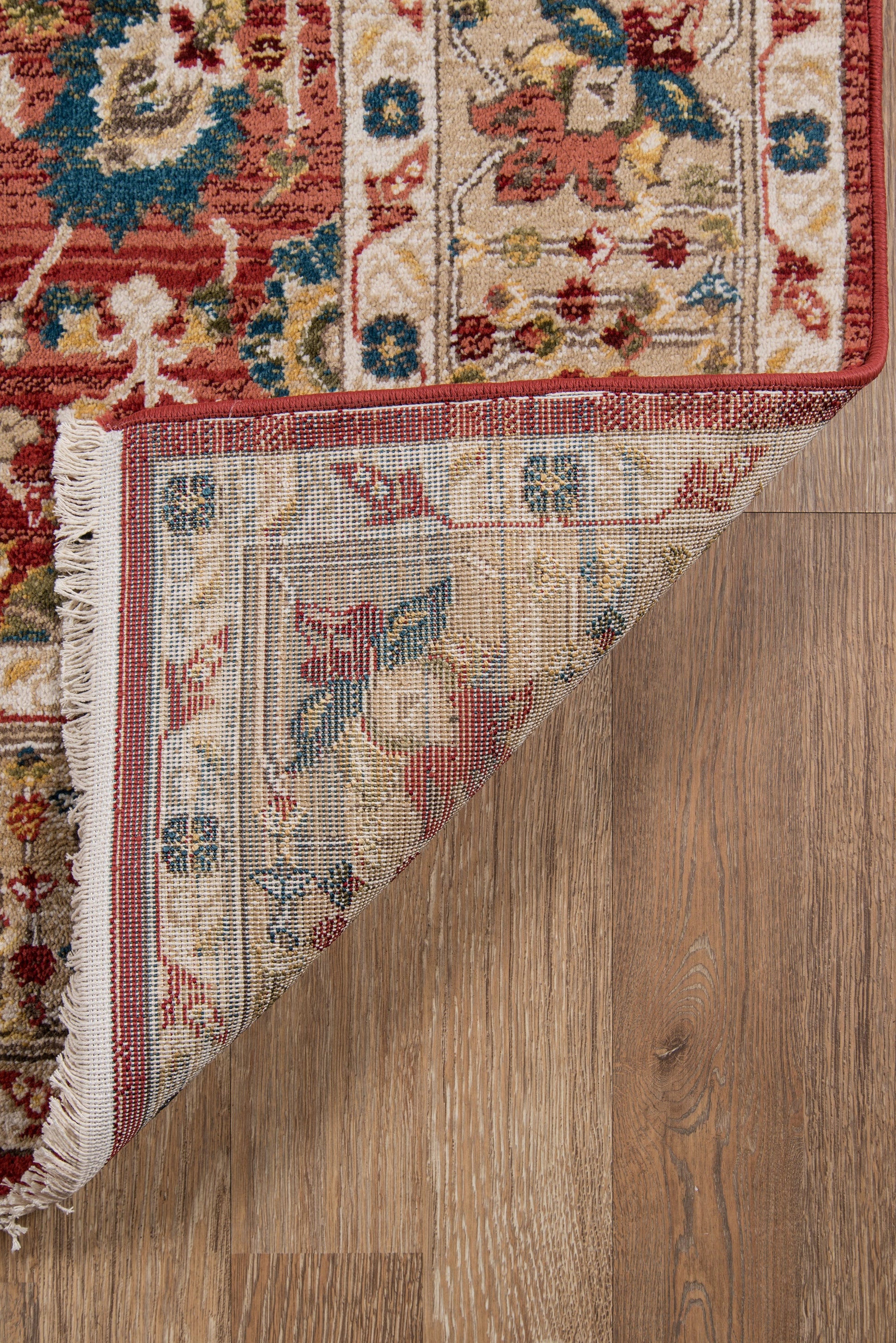 Red traditional oriental rug with floral border; folded corner reveals blue-ivory underside on a wooden floor.