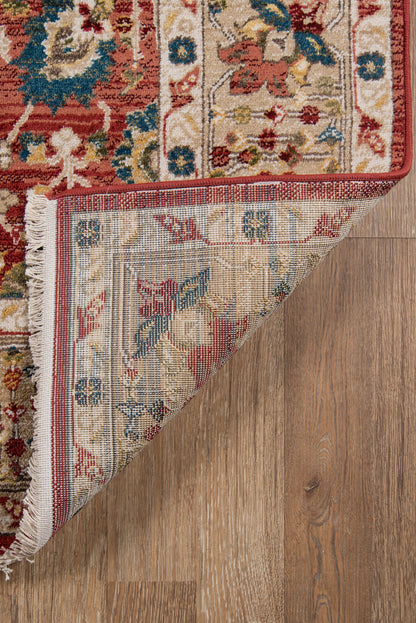 Oriental rug with red border and multicolor floral pattern; folded corner reveals pale blue backing on wood floor.