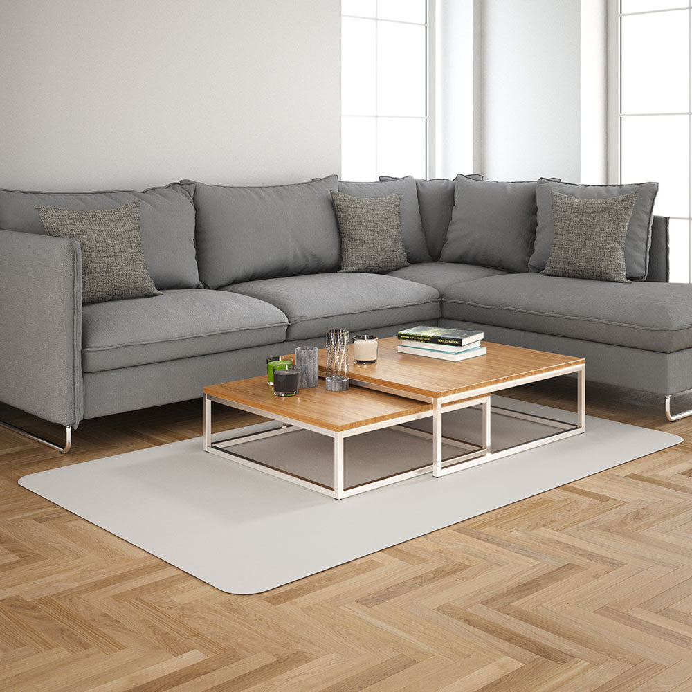 Grey sectional sofa with cushions and light-wood nesting tables with white metal frames on a beige rug in a bright modern living room