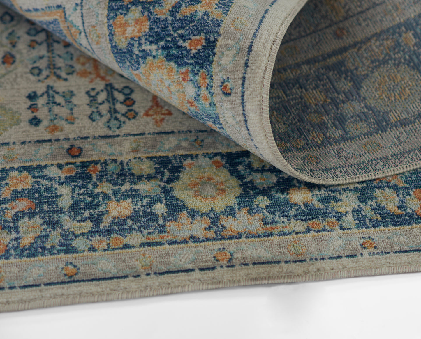 Blue and cream oriental rug with orange floral motifs, partly rolled, woven texture.
