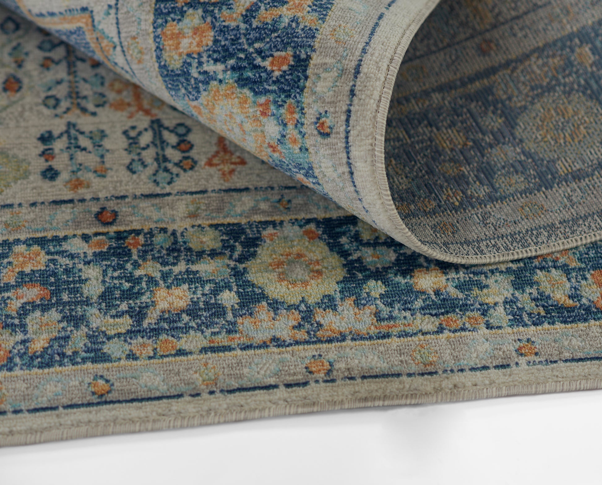 Blue and cream oriental rug with orange floral motifs, partly rolled, woven texture.