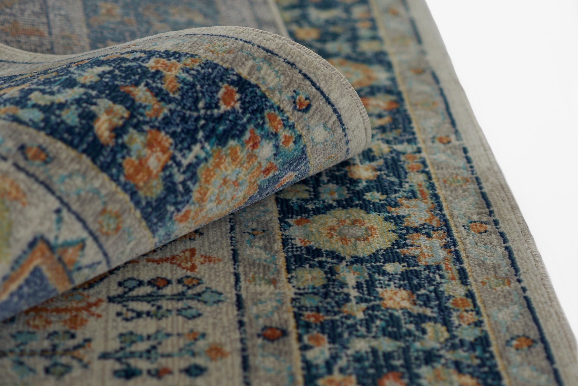 Blue and beige woven Oriental rug with floral patterns, folded corner shows detailed border and orange accents.
