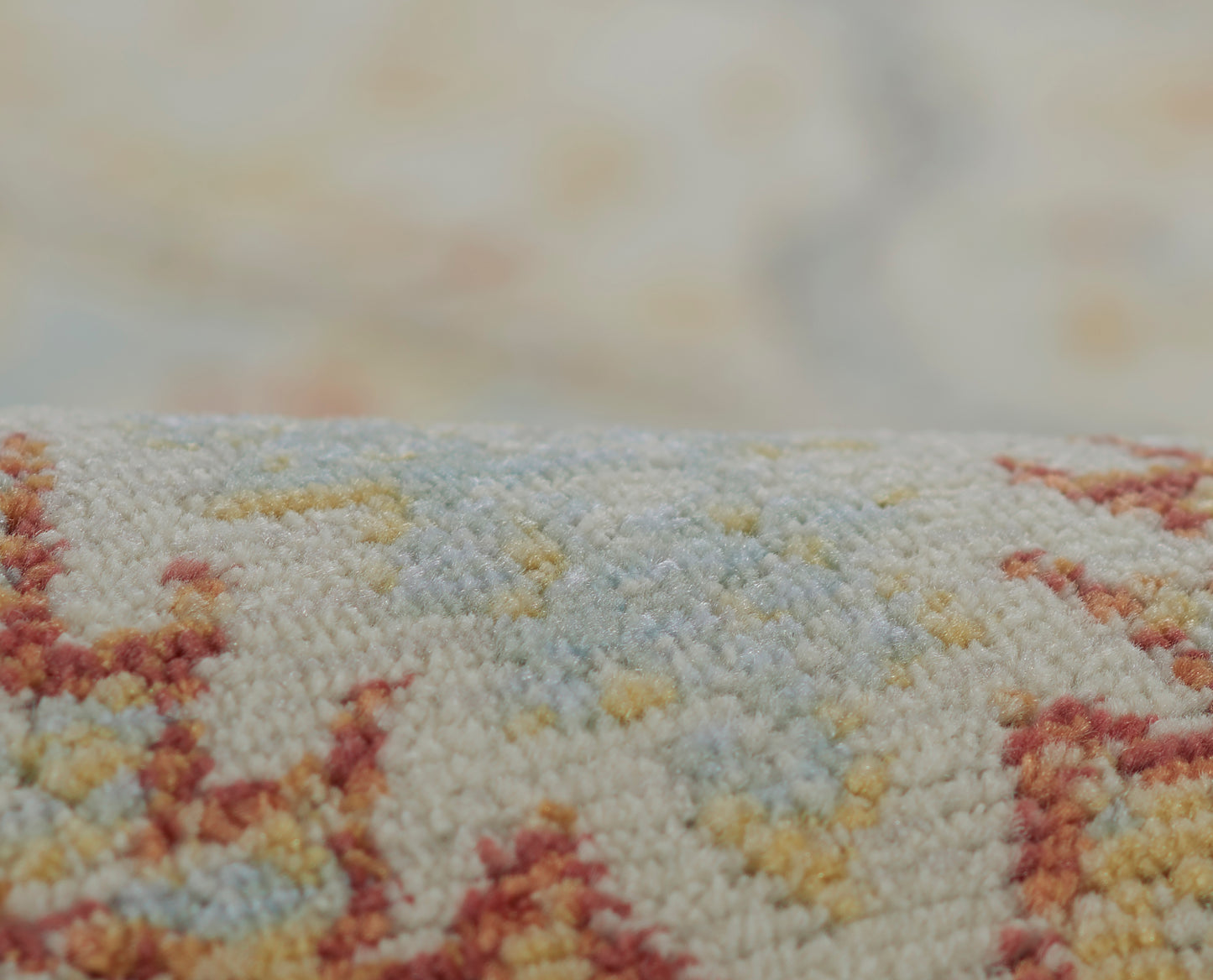 Close-up of a textured woven rug in cream with pale blue, yellow & rust geometric motifs.