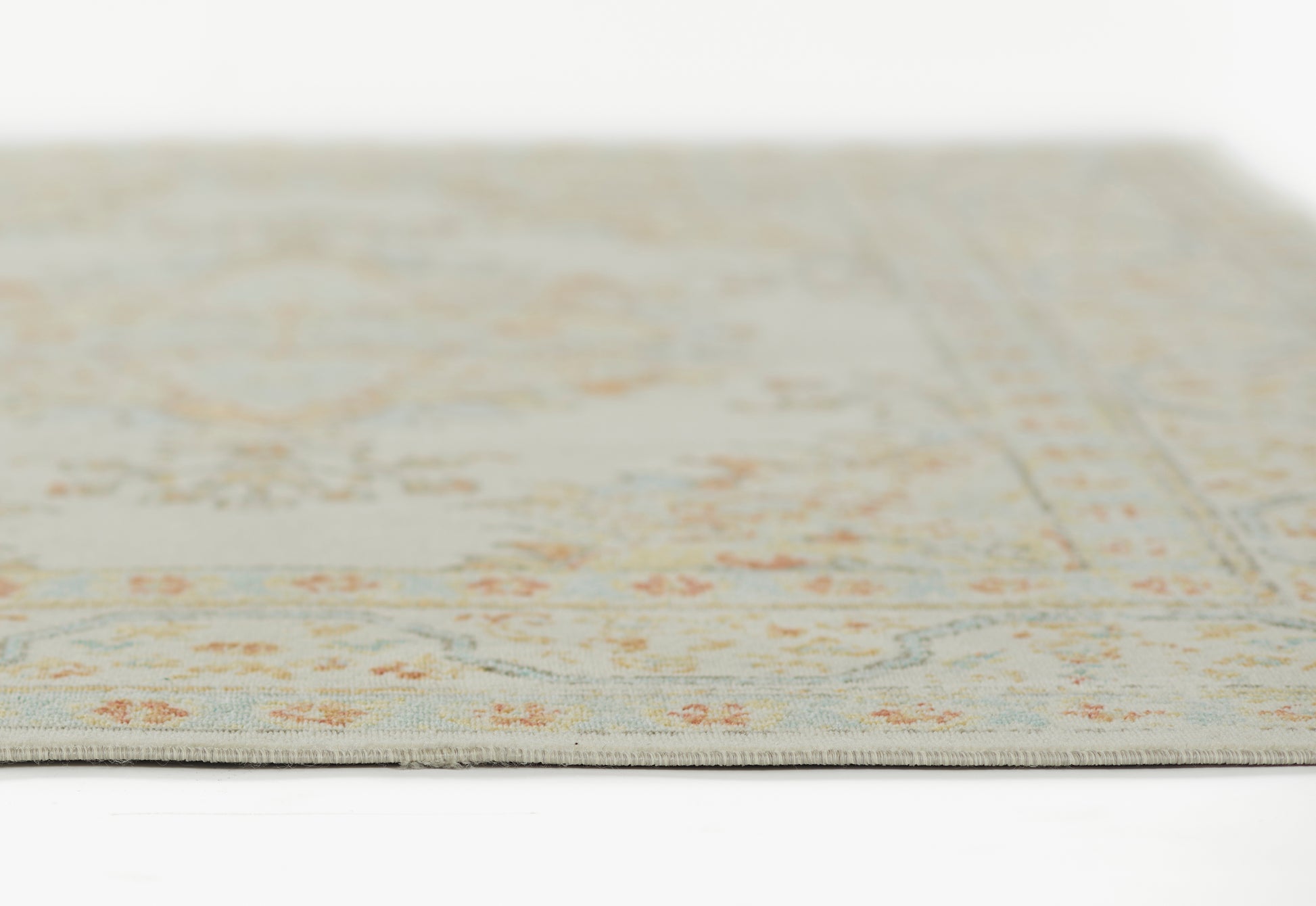 Beige floral area rug (2' x 3') with subtle blue & orange accents, close-up edge view, soft low-pile fabric.