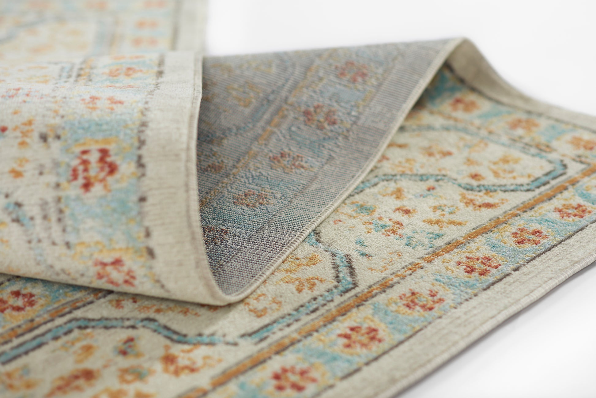 Floral patterned rug in blue, beige and orange with a light grey border; woven texture and folded edge.