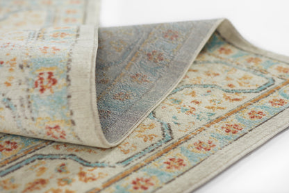 Floral patterned rug in blue, beige and orange with a light grey border; woven texture and folded edge.
