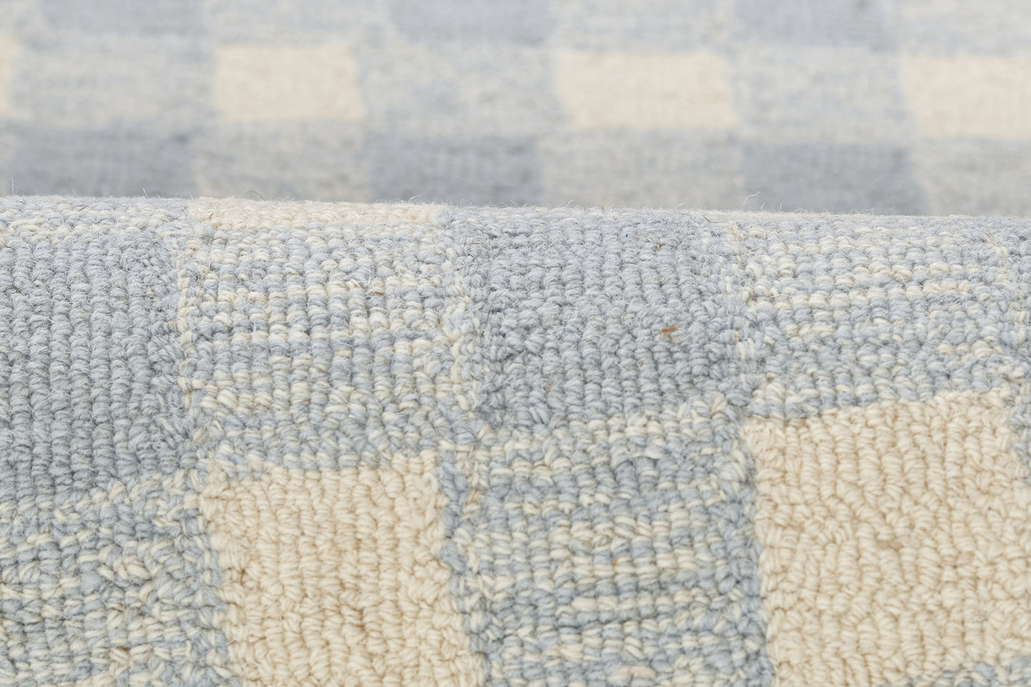 Close-up of a light blue and cream checkered woven rug texture with a soft looped pile.