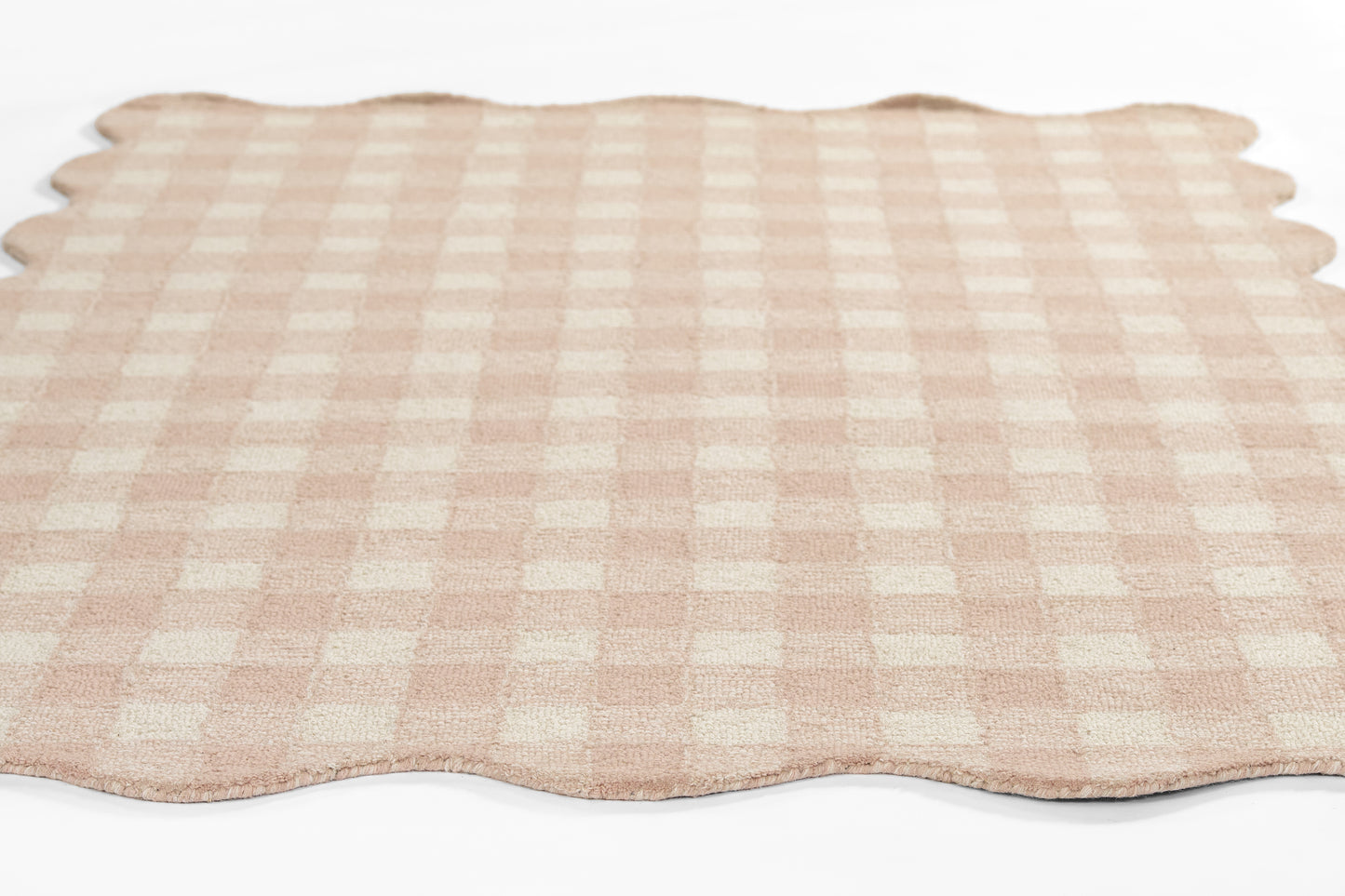 Beige and pink gingham rug with scalloped edges, laid flat.