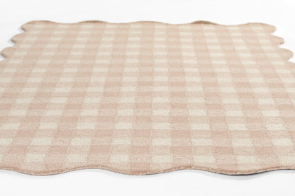Beige and pink gingham rug with scalloped edges, laid flat.
