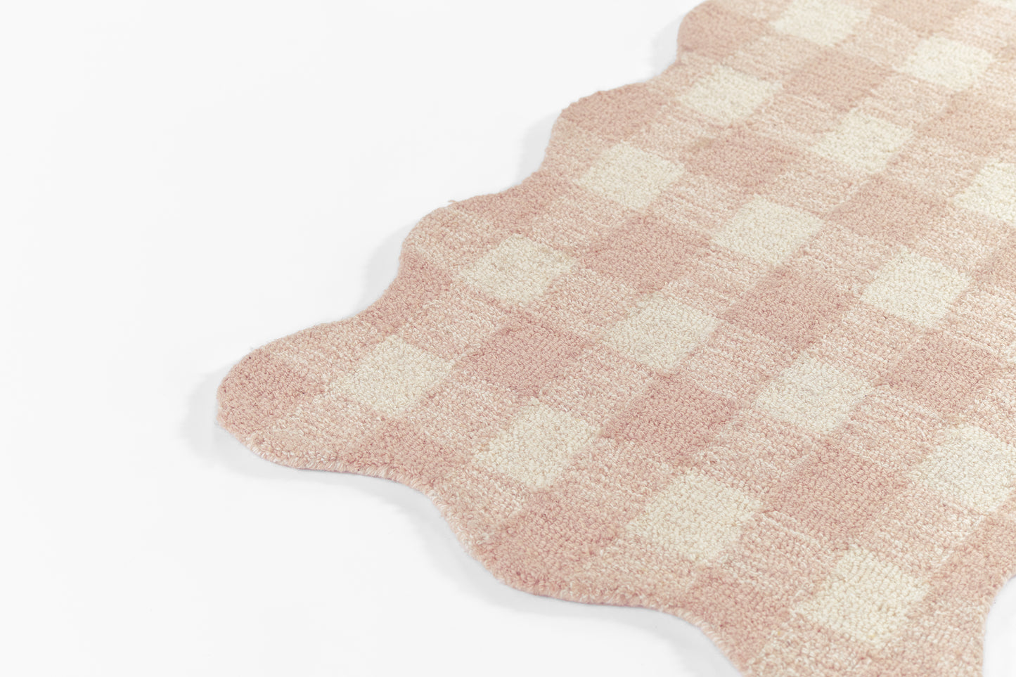 Soft pink and cream checkered rug with scalloped edge and plush woven texture