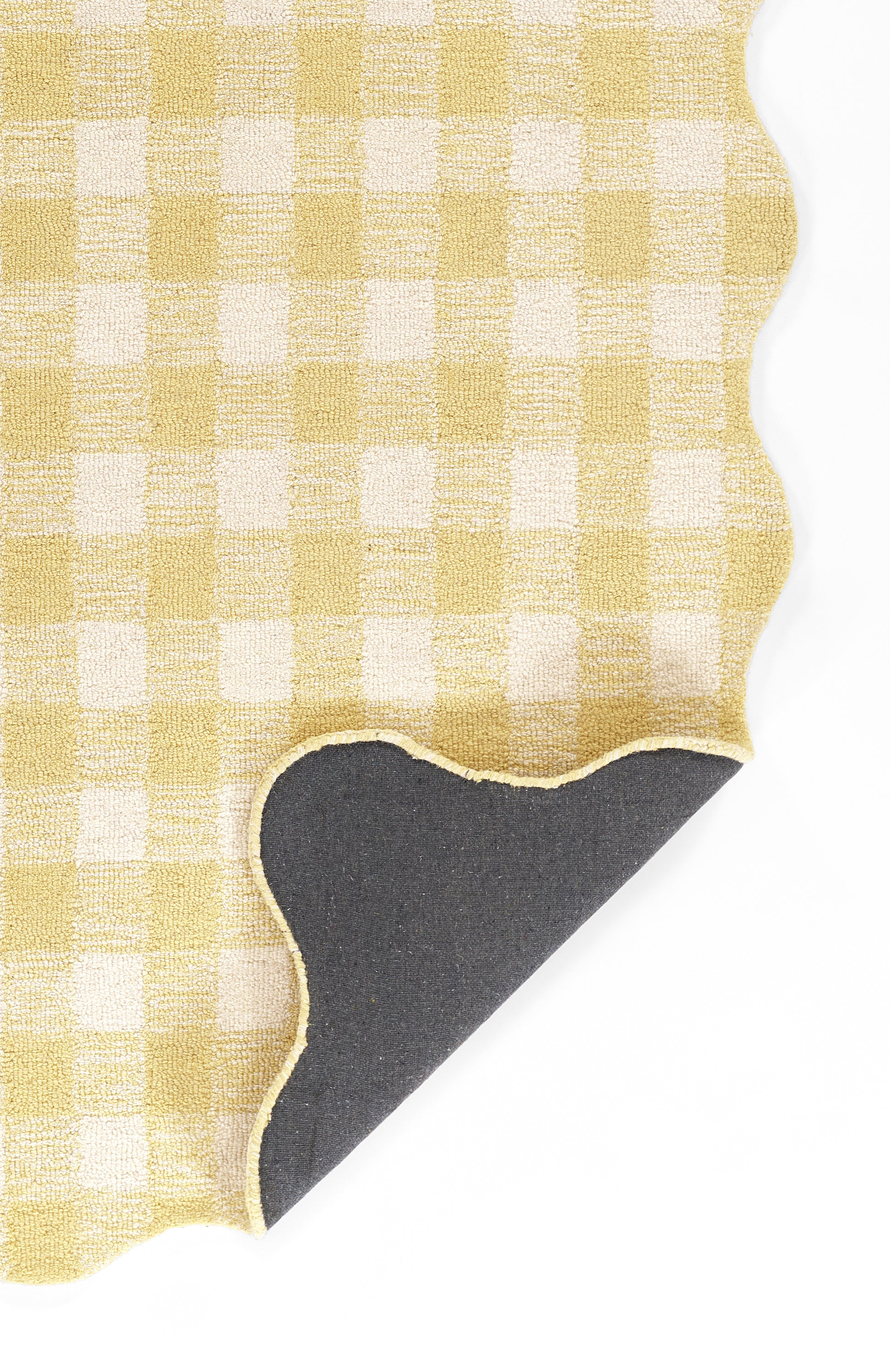 Yellow gingham rug with a scalloped white border; a dark curved shape peeks from underneath.