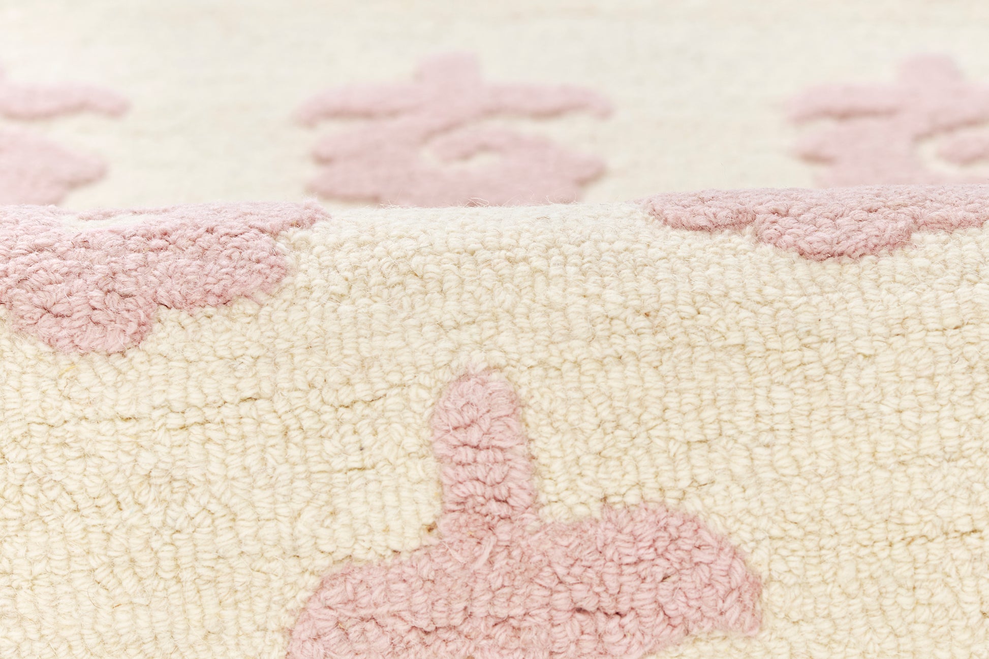 Close-up of cream plush rug with pink bunny silhouettes; soft looped texture, cozy kids' decor.