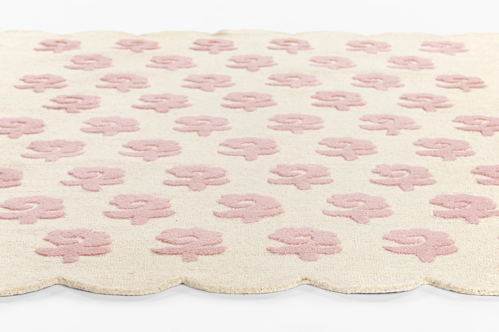 Cream rug with pale pink four-petal flower motifs and a scalloped edge.
