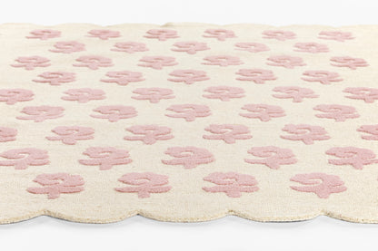 Cream bath rug with pink four-leaf-clover motifs, plush terry texture and scalloped edge.