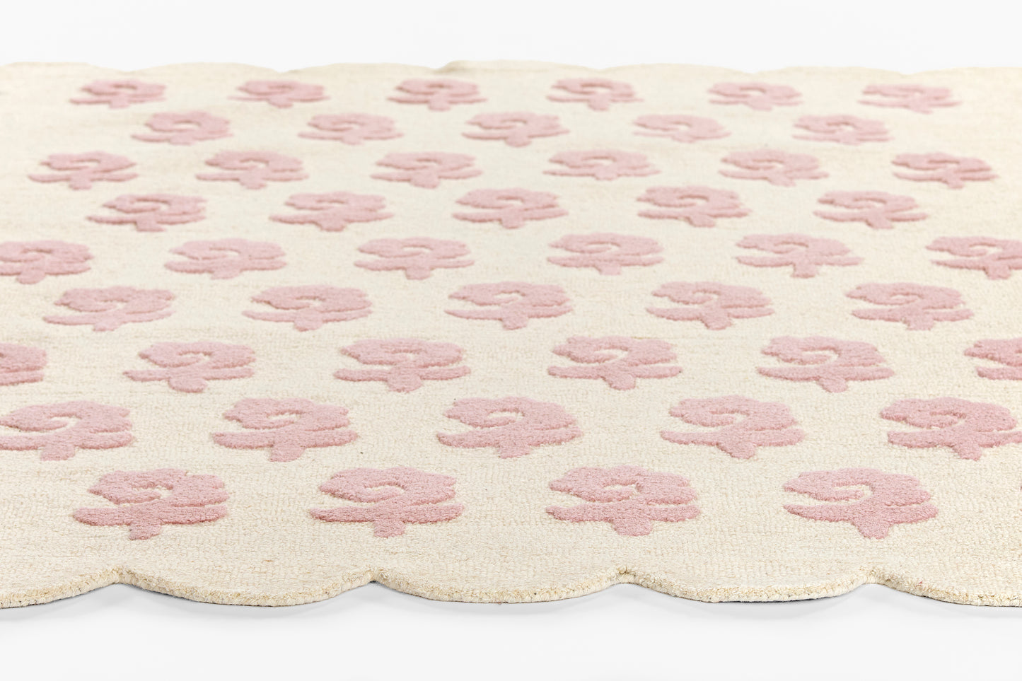 Cream rug with pink four-petal flower motifs & scalloped edge.