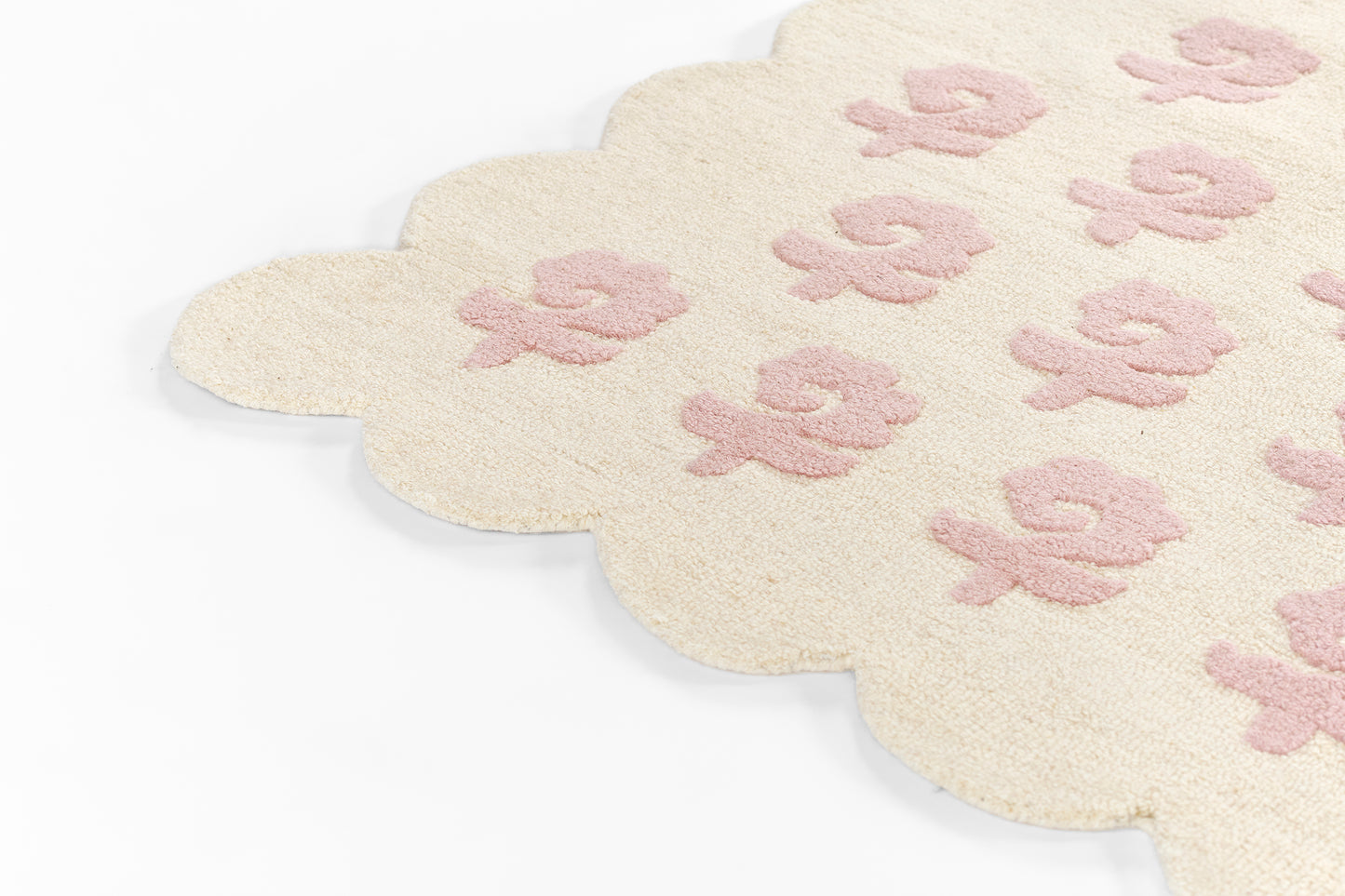 Cream scalloped rug with pale pink flower motifs and soft plush texture.