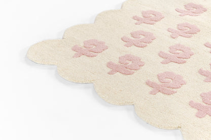 Cream scalloped-edge rug with pink lily floral motifs, plush textured fabric, decorative home accent.