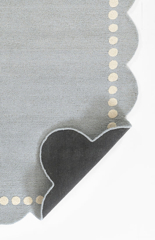 Blue-gray linen-like rug with scalloped edge and beige dotted trim, featuring a dark heart-shaped corner accent, 8' x 10'.