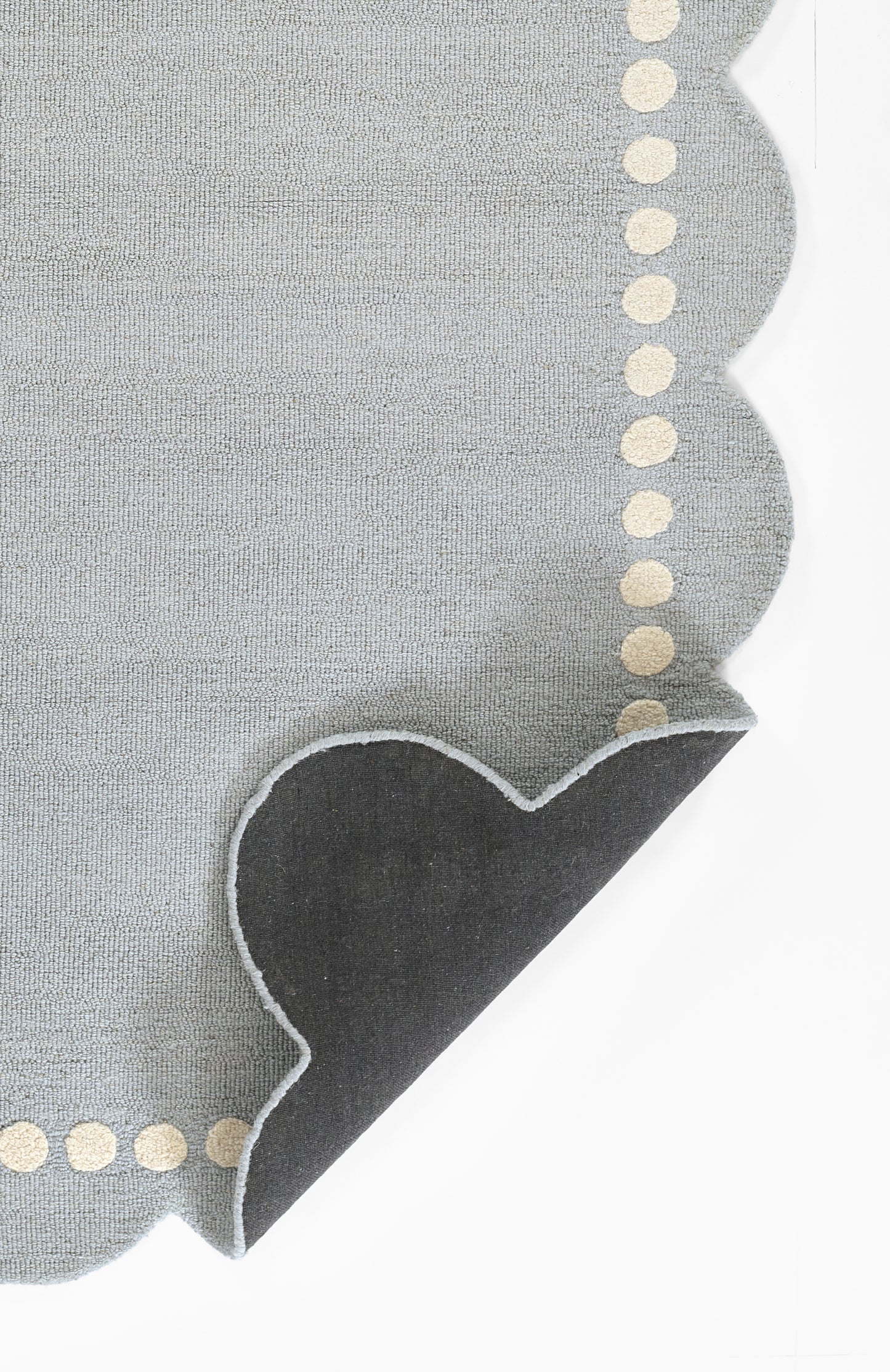 Blue-gray rug with a scalloped edge, cream dot trim, and a dark heart applique at a corner.