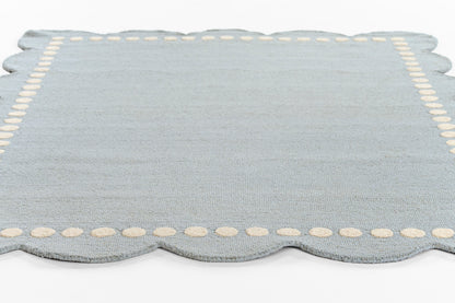 Light blue scalloped-edge rug with cream dotted border; soft textile for living room.