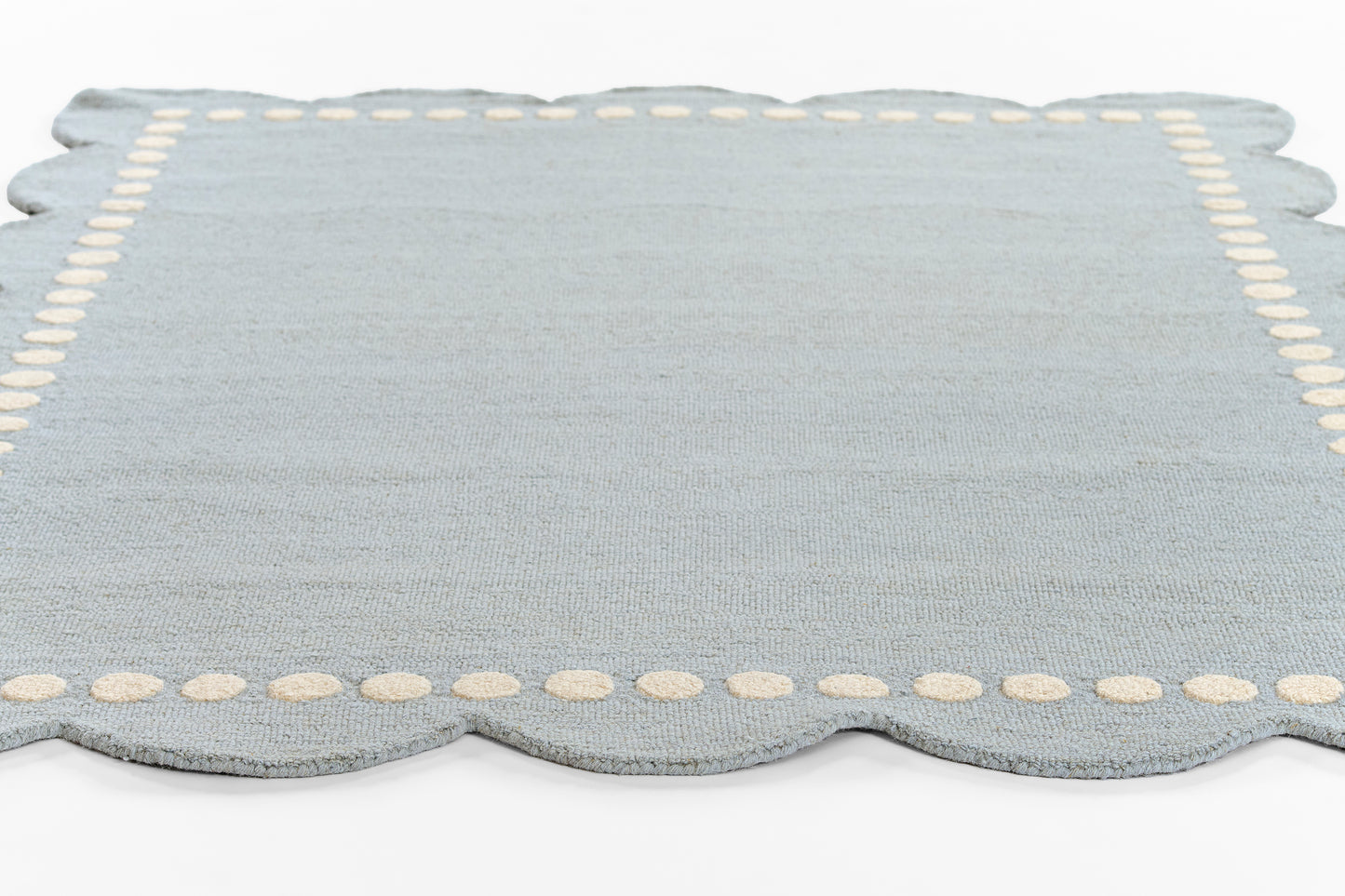 Soft blue woven rug with cream border dots and scalloped edge; indoor decorative use.