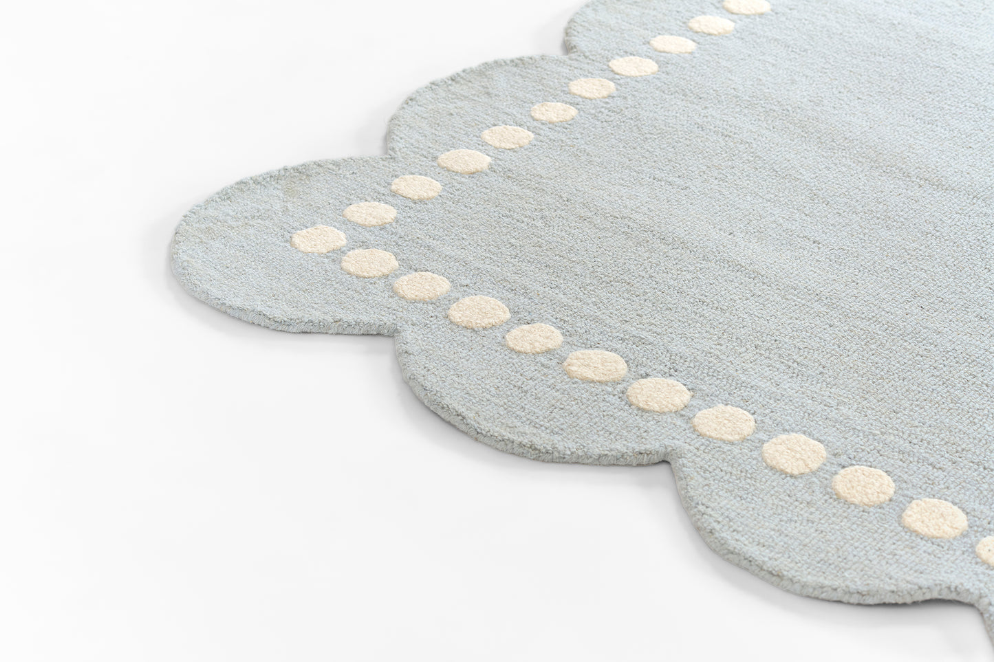 Light blue scalloped rug with cream border dots along the edge; plush, textured surface.