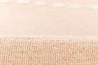 Beige textured loop-pile rug close-up with soft tan fibers, subtle dot pattern, rolled edge visible.