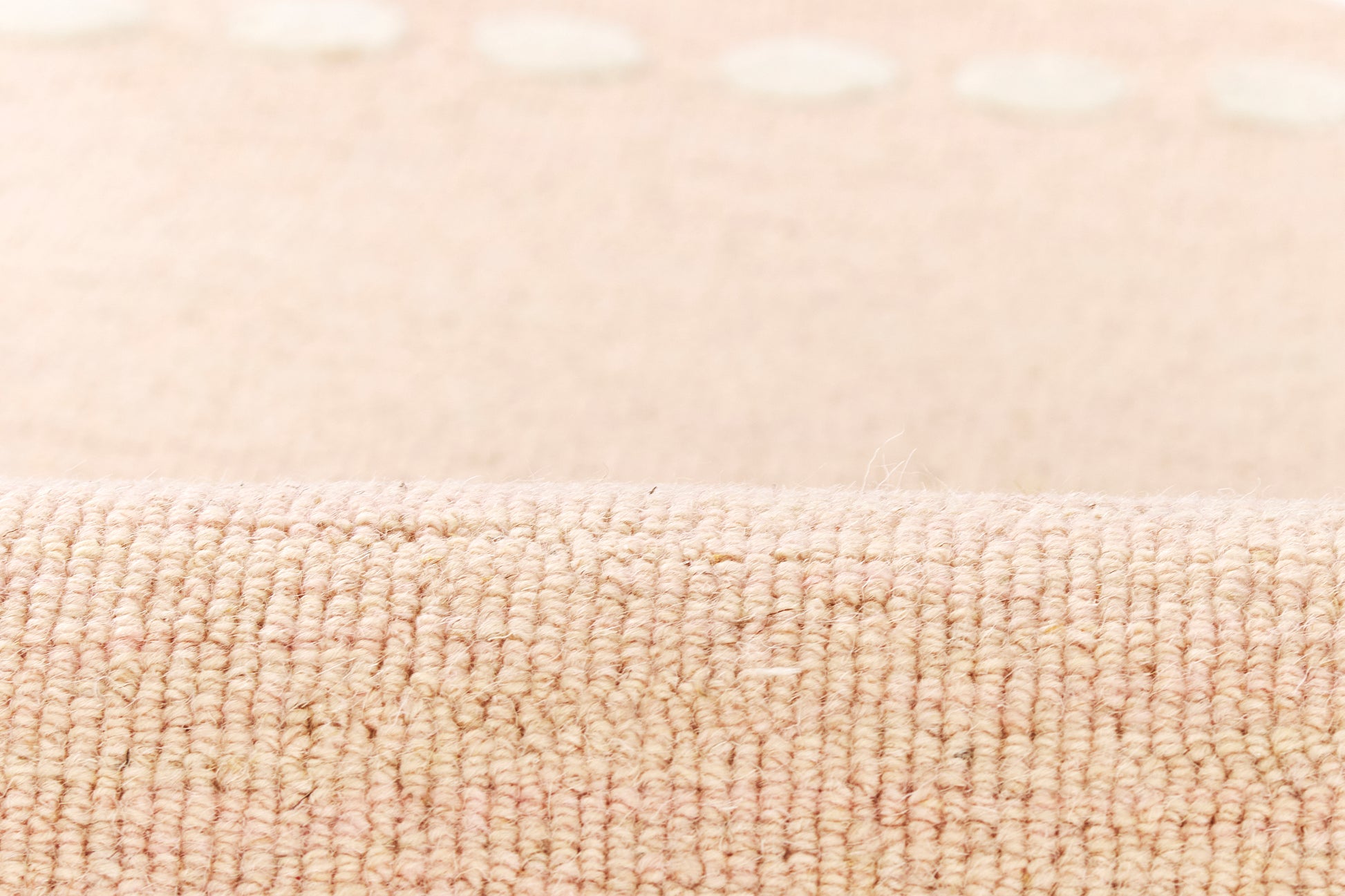 Beige textured rug close-up with looped pile and subtle white dot border along edge.