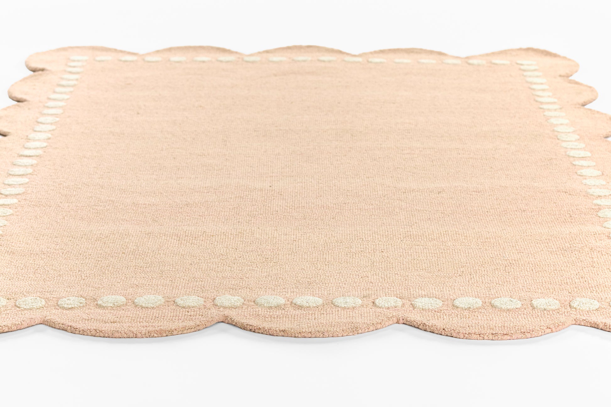 Peach woven rug with scalloped edges and dotted white stitch trim, 9' x 12'.