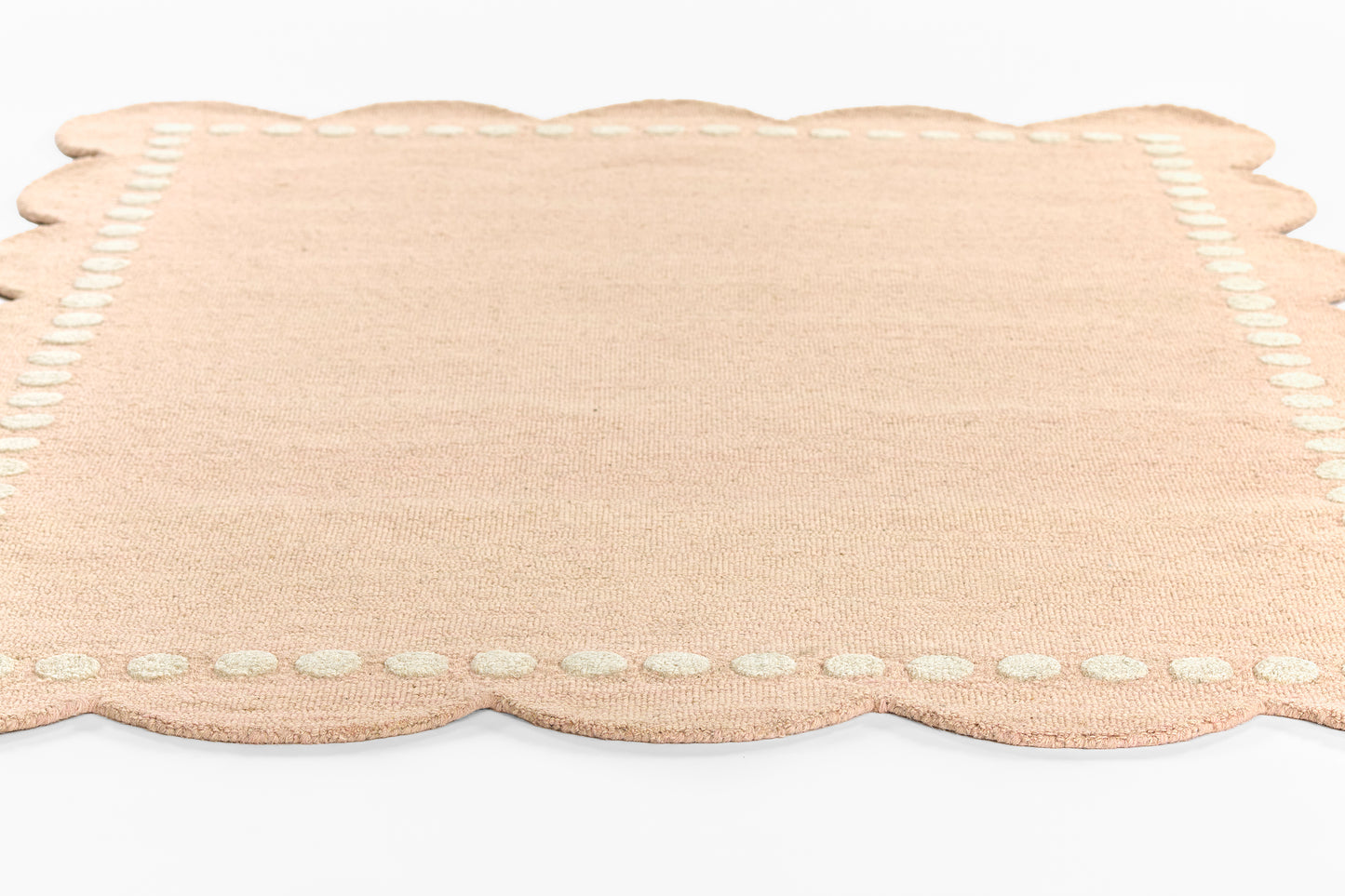 Peach rug with scalloped edge, white stitched border and soft woven texture.