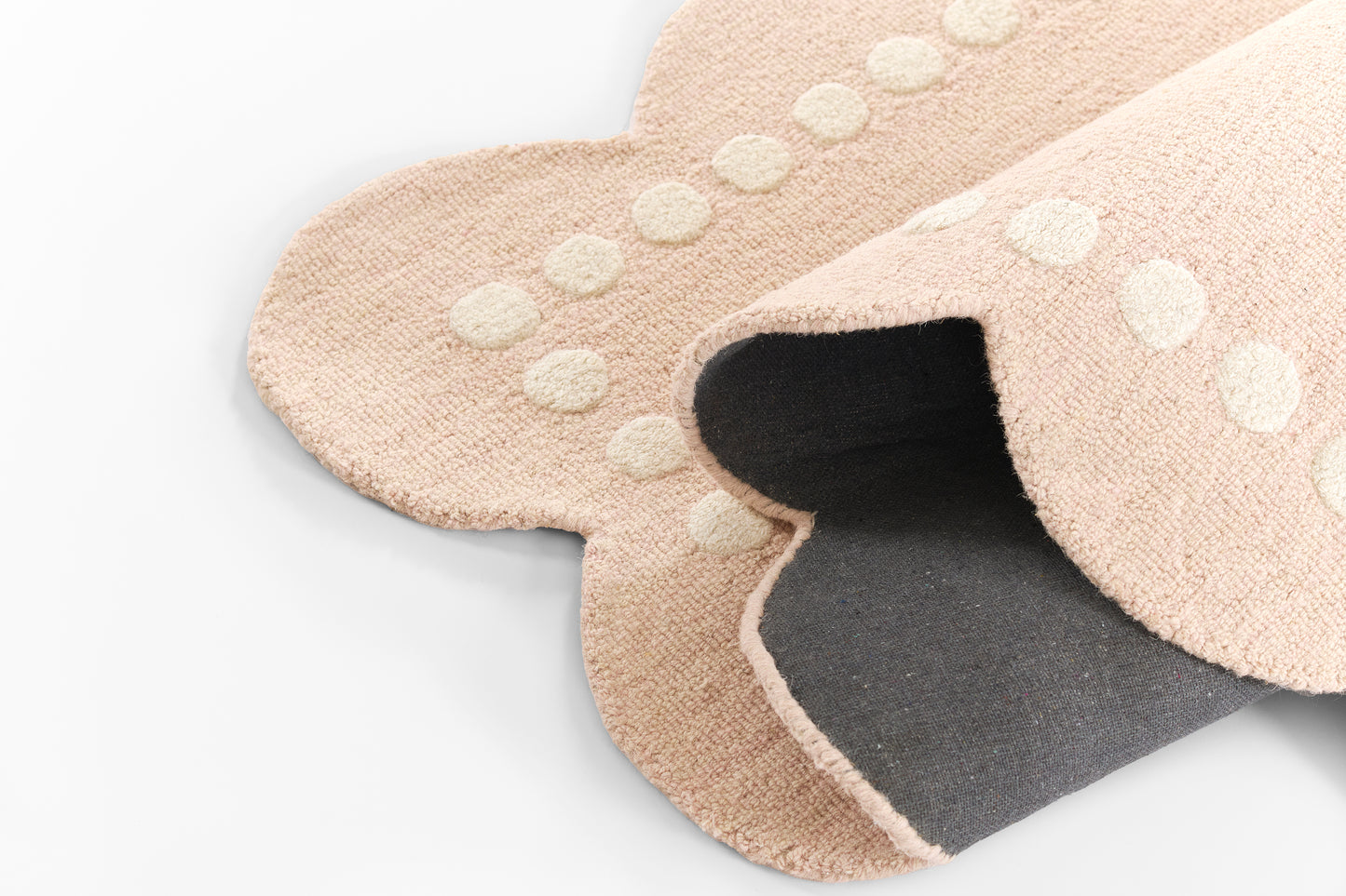 Beige round rug with white polka-dot trim and dark inner lining, soft fuzzy fabric.