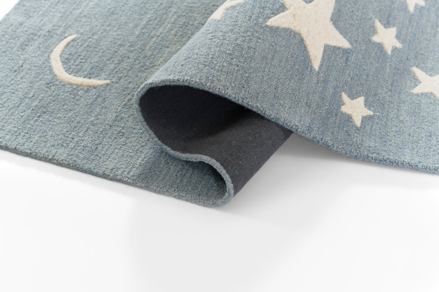 Blue textured rug with white stars and crescent moons, soft pile, rolled corner showing underside.