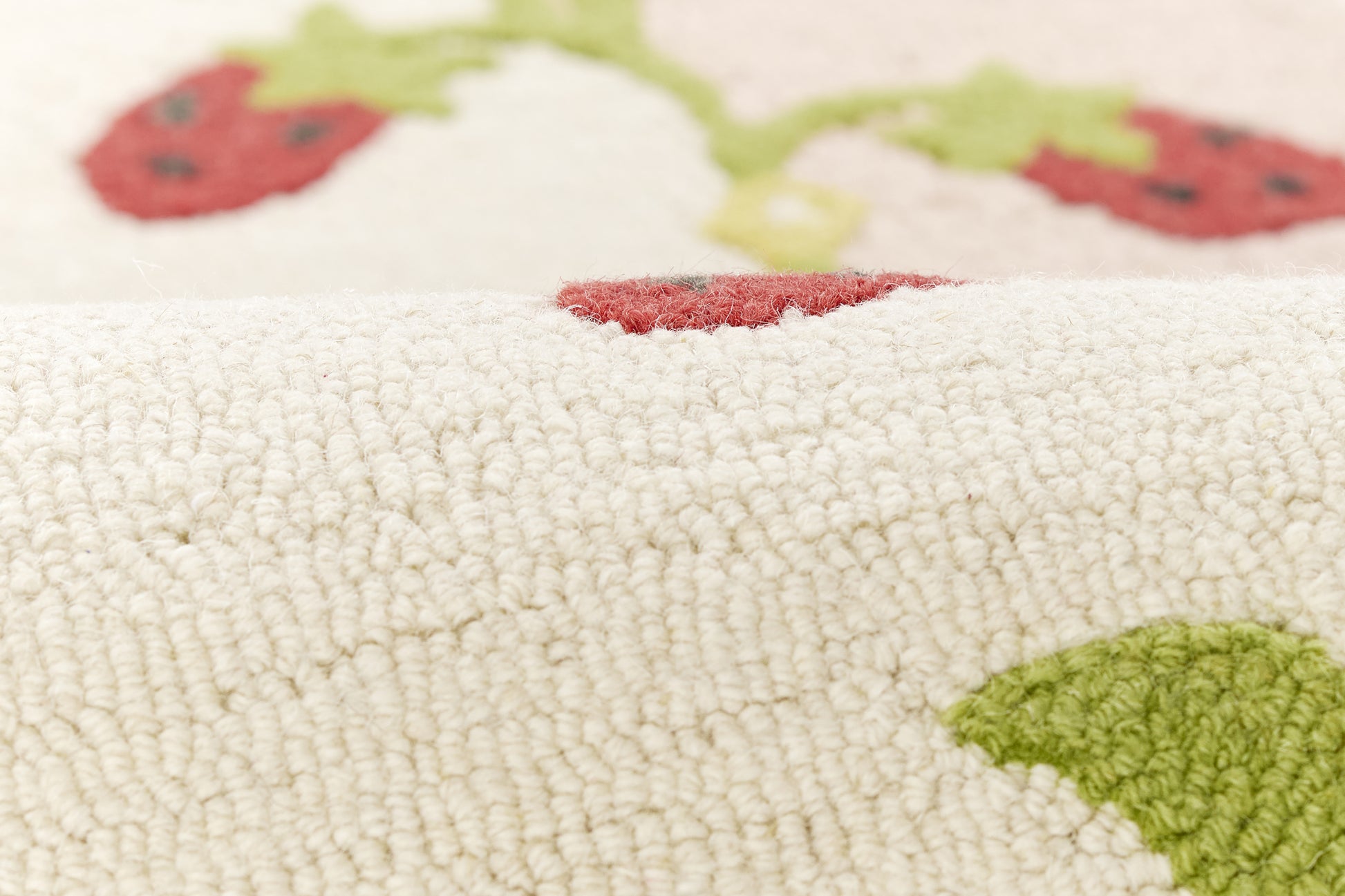Cream rug with red flowers and green leaves; close-up of plush looped texture.