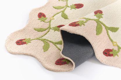 Beige floral-patterned rug with green vines and red berries, scalloped edge, rolled corner showing gray backing.