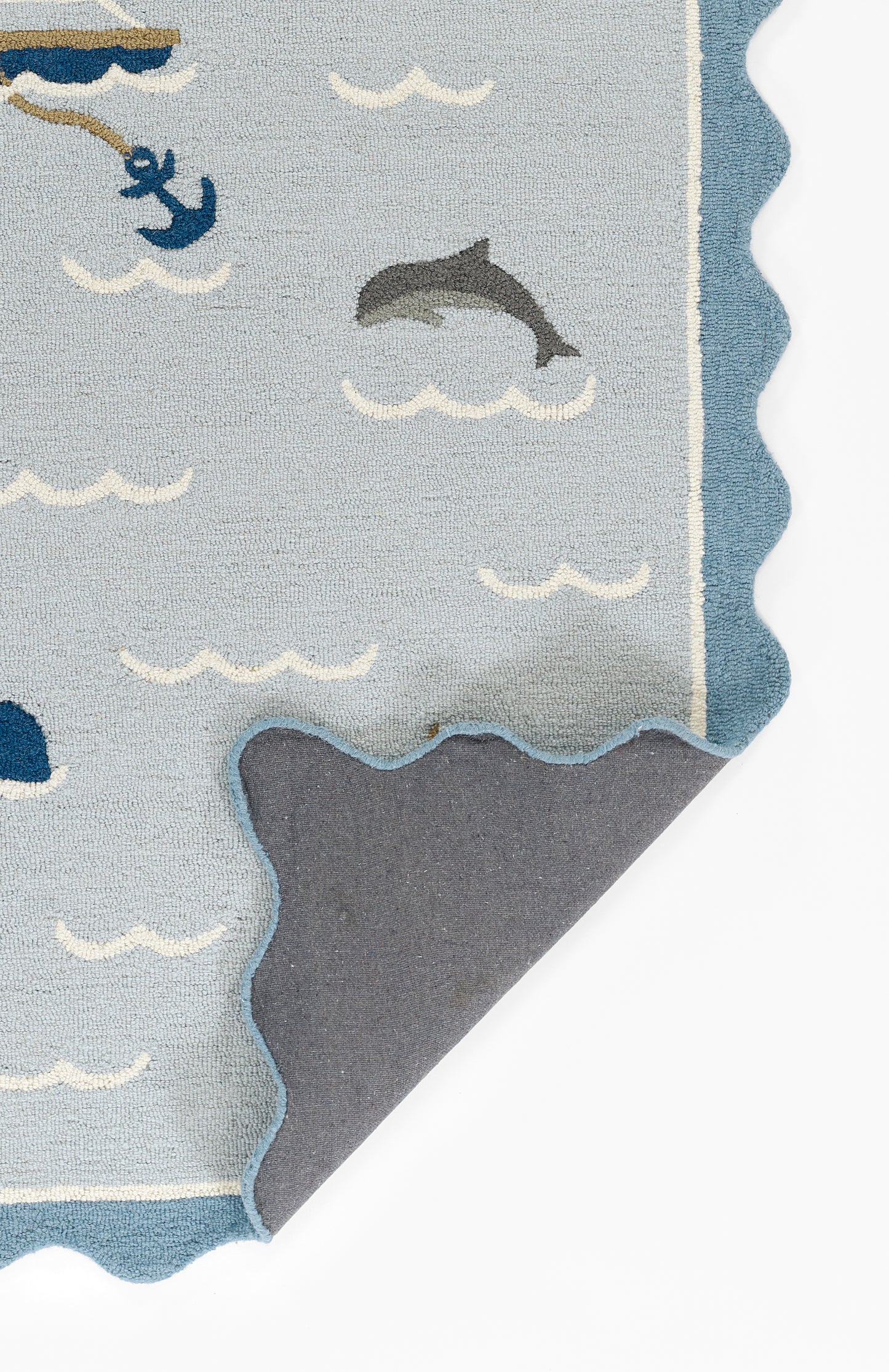 Light blue coastal rug with dolphins, anchors and white wave motifs; scalloped navy border, soft textile.