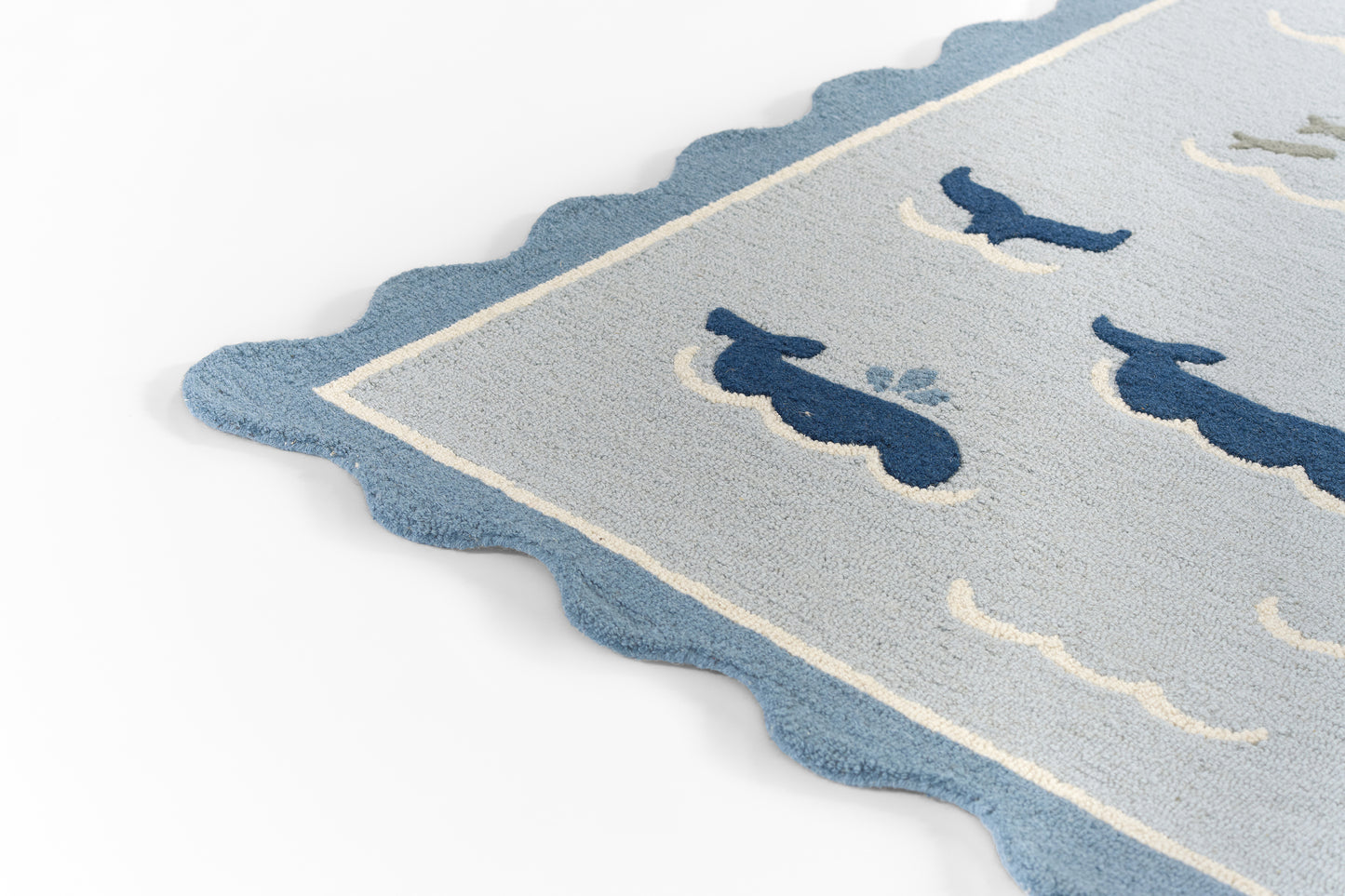 Light blue scalloped-edge rug with dark navy whale silhouettes and pale border, coastal style.