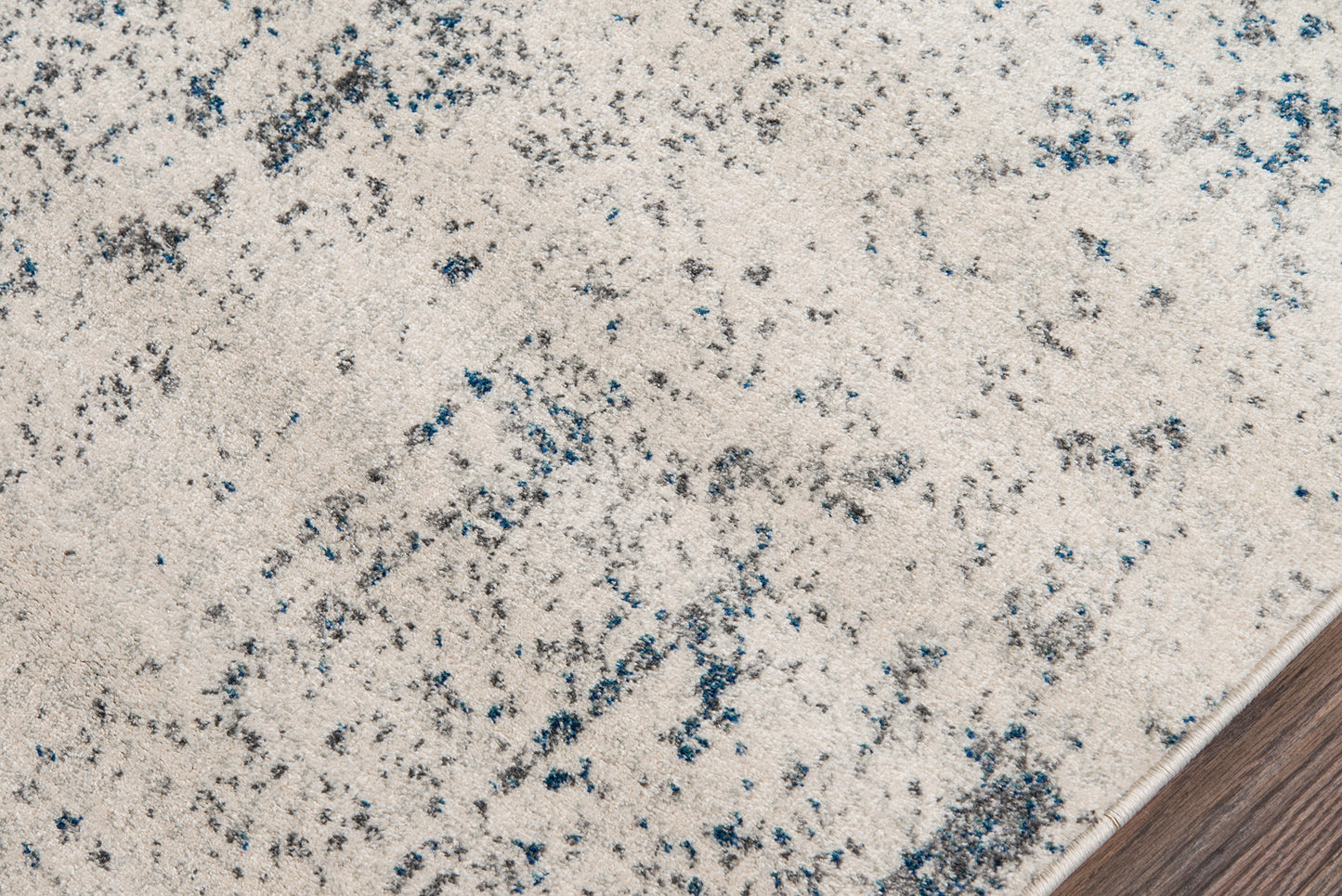 Ivory speckled area rug with blue-gray flecks, close-up edge against wood floor