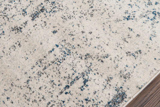 Ivory speckled area rug with blue-gray flecks, close-up edge against wood floor