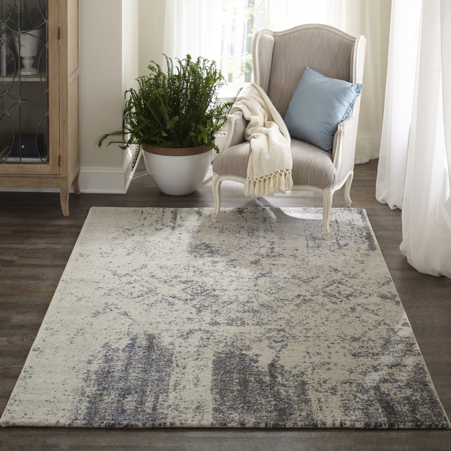 Cream woven area rug with gray-blue distressed pattern in a cozy living room with a beige wing chair and blue pillow.