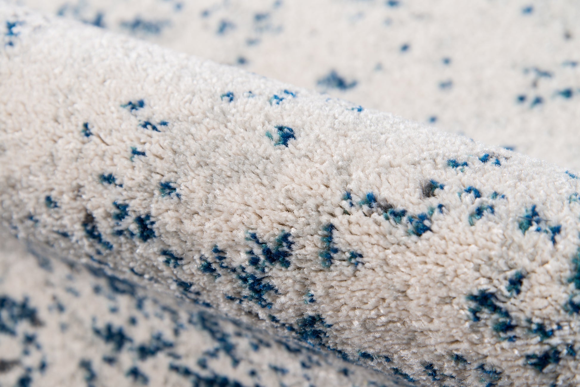 Cream shag rug with blue speckled pattern & plush textured pile; modern abstract design.