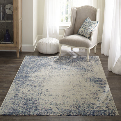 Blue and ivory distressed-pattern rectangular rug, low-pile, in a light-filled living room with a beige wingback chair and white pouf.