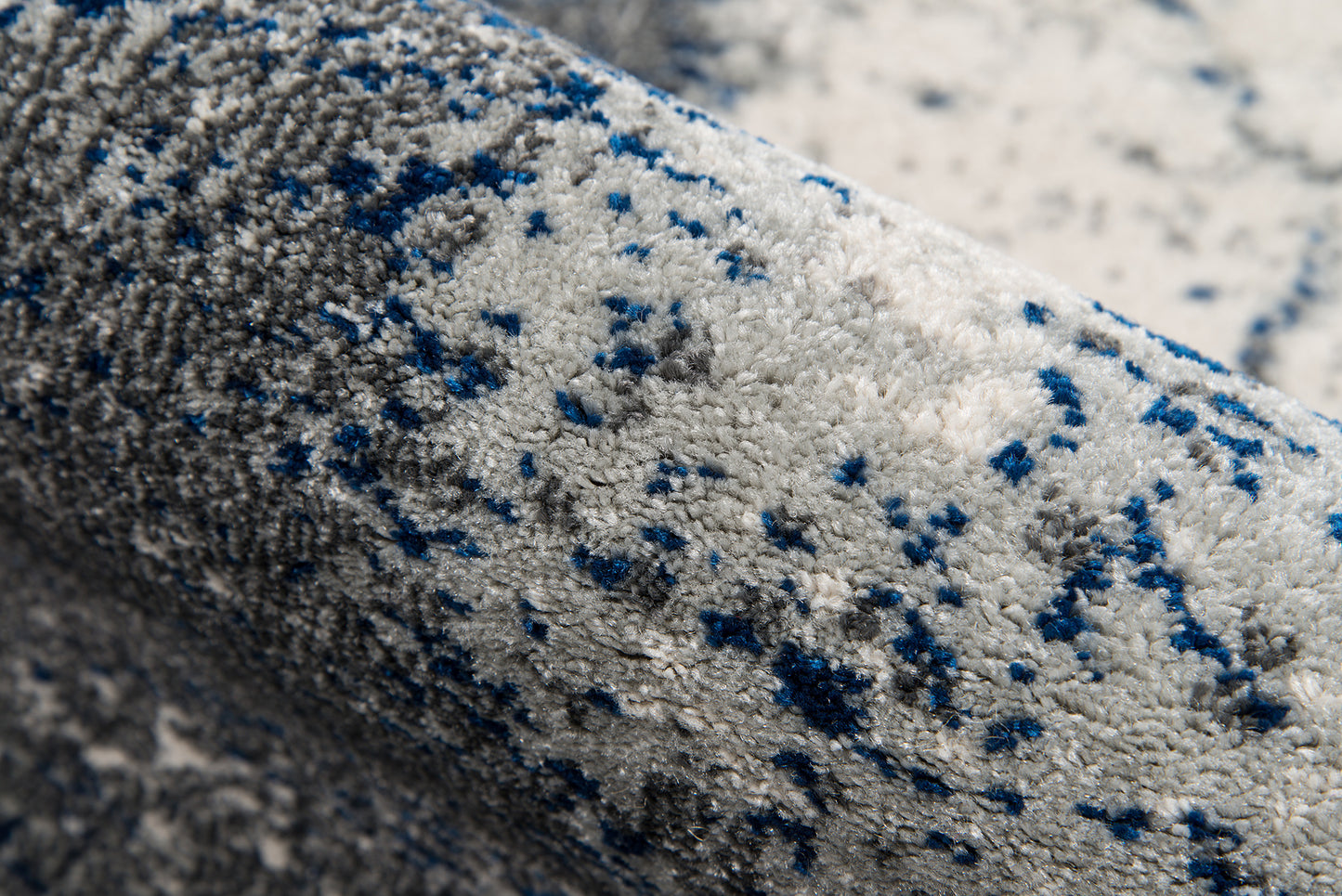 Rolled gray plush rug with blue speckles; soft pile and modern speckled style.