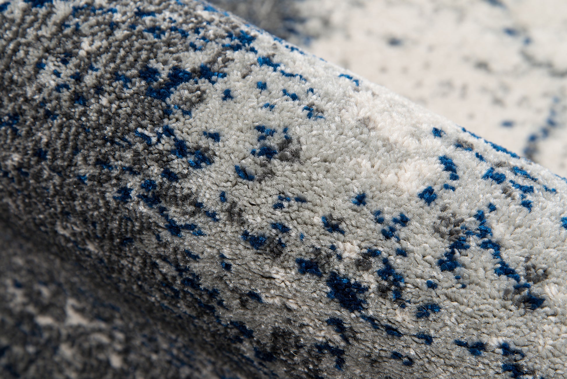 Rolled gray plush rug with blue speckles; soft pile and modern speckled style.