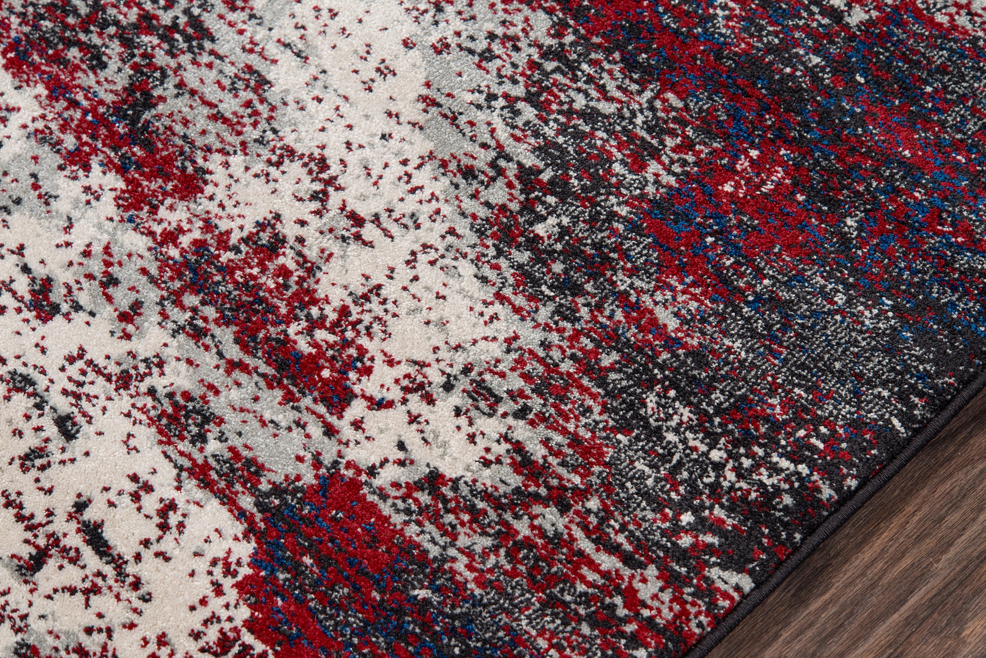 Abstract area rug with cream base and red, blue, gray speckle pattern; edge on dark wood floor.