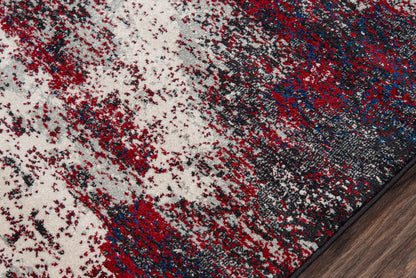 Abstract gray rug with red and navy blue splatters on a dark wood floor edge.