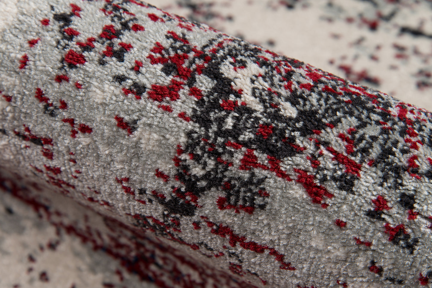 Rolled gray area rug with red, black and ivory speckled abstract pattern; plush textured pile.