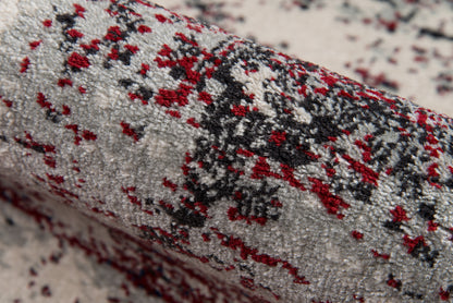 Close-up of a gray shag rug with red and black speckled abstract pattern; plush, modern decor.