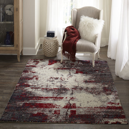 Abstract distressed rug in red, gray, and ivory beside a gray upholstered armchair with a red throw and white fluffy pillow.